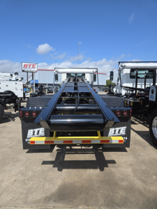 Rolloff truck rear showing BTE branding and reflective strip, with a hydraulic hooklift frame and bumper lights.