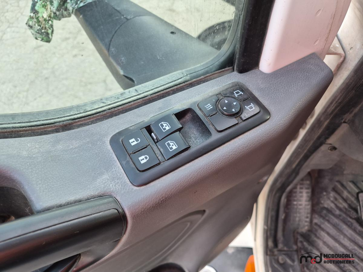 Truck cab interior showing window/side mirror controls panel on door, with window switch buttons and a round joystick control.