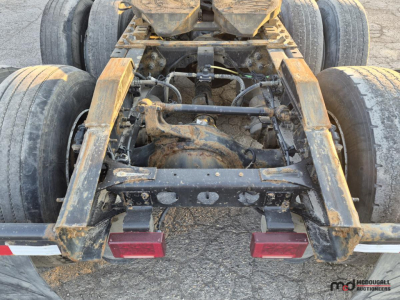 Tractor-trailer chassis view showing rear drive axles and hitch assembly with rusty steel frame and two red taillights.