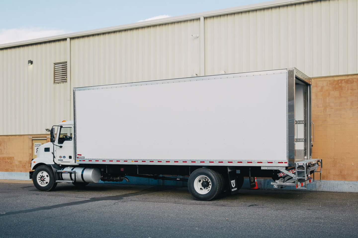 Box truck side view showing a white 2025 Mack MD6 with a large box body, cab at left, long trailer, and no visible branding on the box.