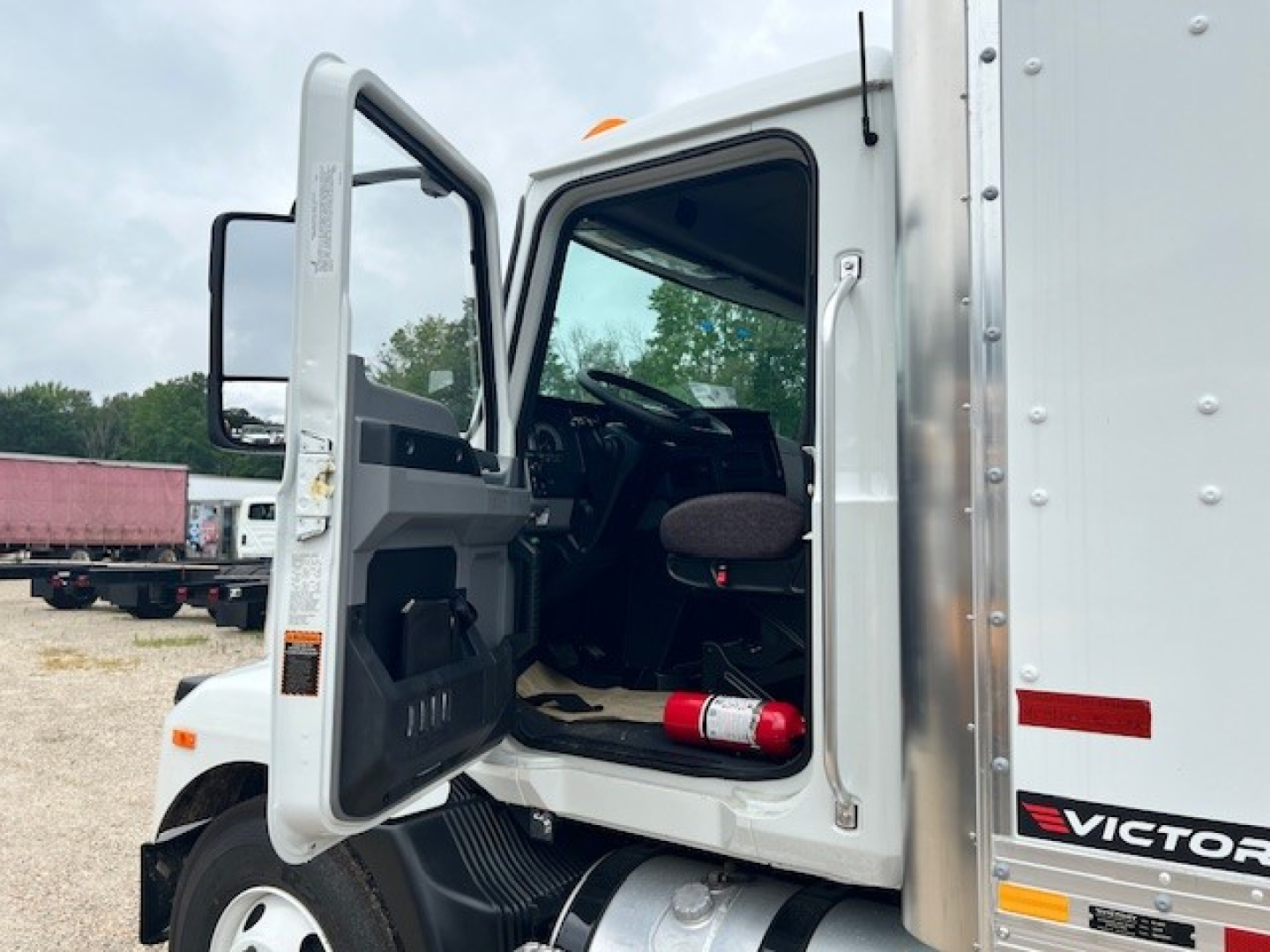 Truck cab interior visible through open driver's door of a new 2025 Mack MD6 with a fire extinguisher in the cabin.