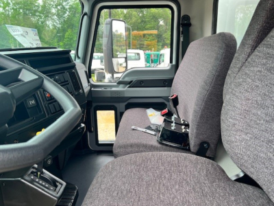 Cab interior of a 2025 Mack MD6 truck showing driver seat and dashboard; steering wheel, control panel, and door with window; center console and gear selector visible.
