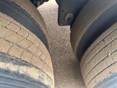 Dual rear trailer tires with dusty tread and mud on pavement.