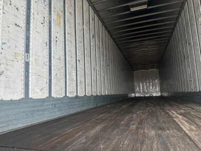 Empty utility trailer interior showing wood floor and ribbed metal sides, front bulkhead, and dim lighting.