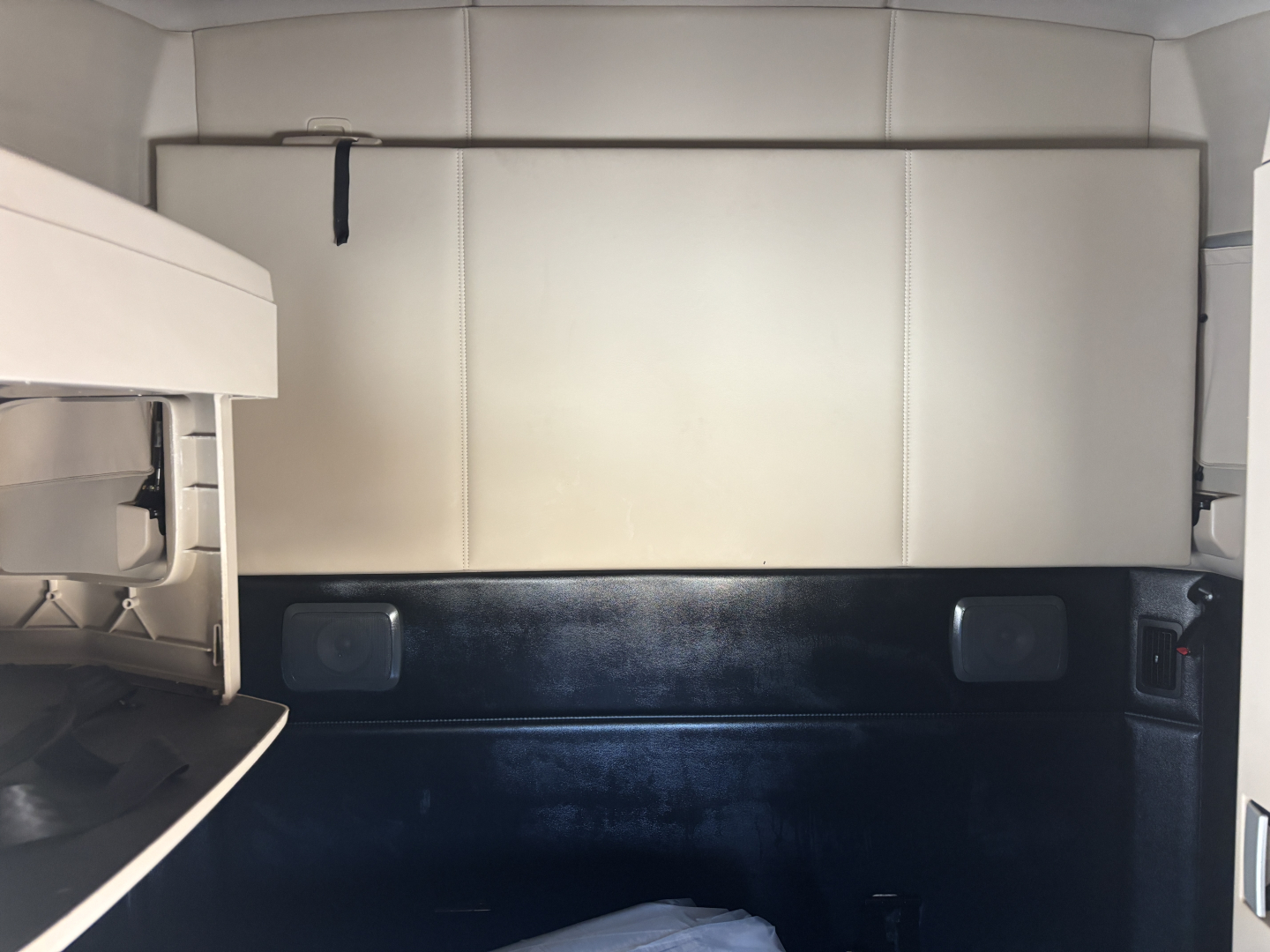 Kenworth T680 sleeper cab interior cargo area with light-colored panels and black lower wall; storage compartments visible.