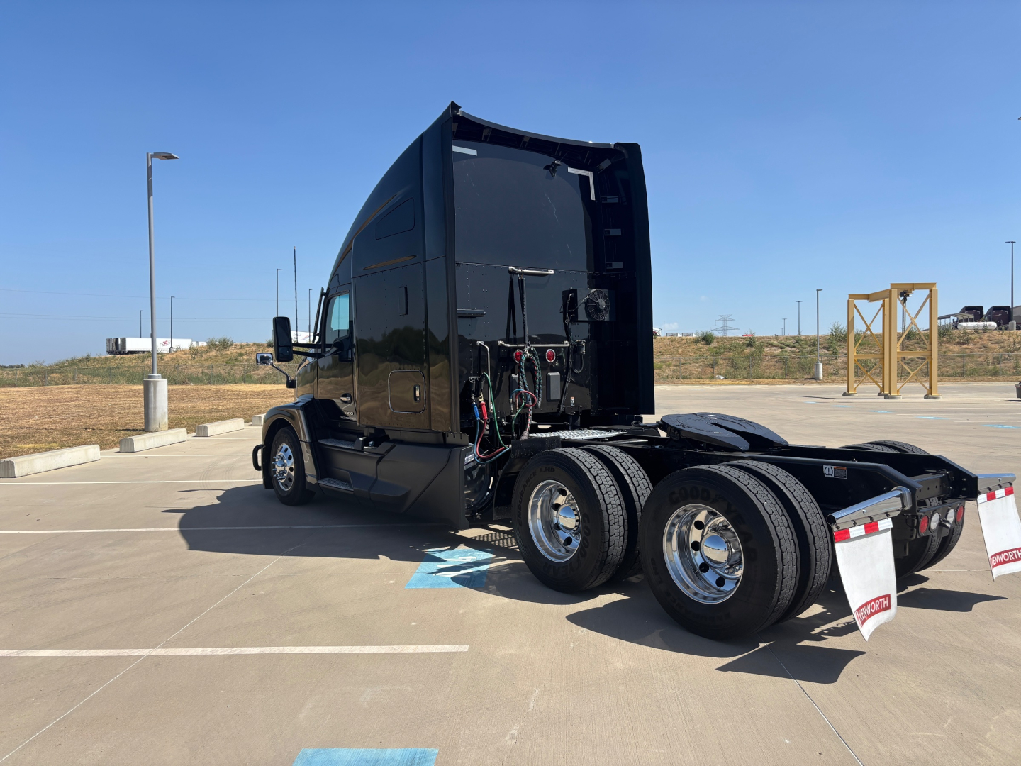 Kenworth T680 tractor rear side view showing fifth-wheel and dual rear axles in a parking lot with black paint and trailer connections visible.