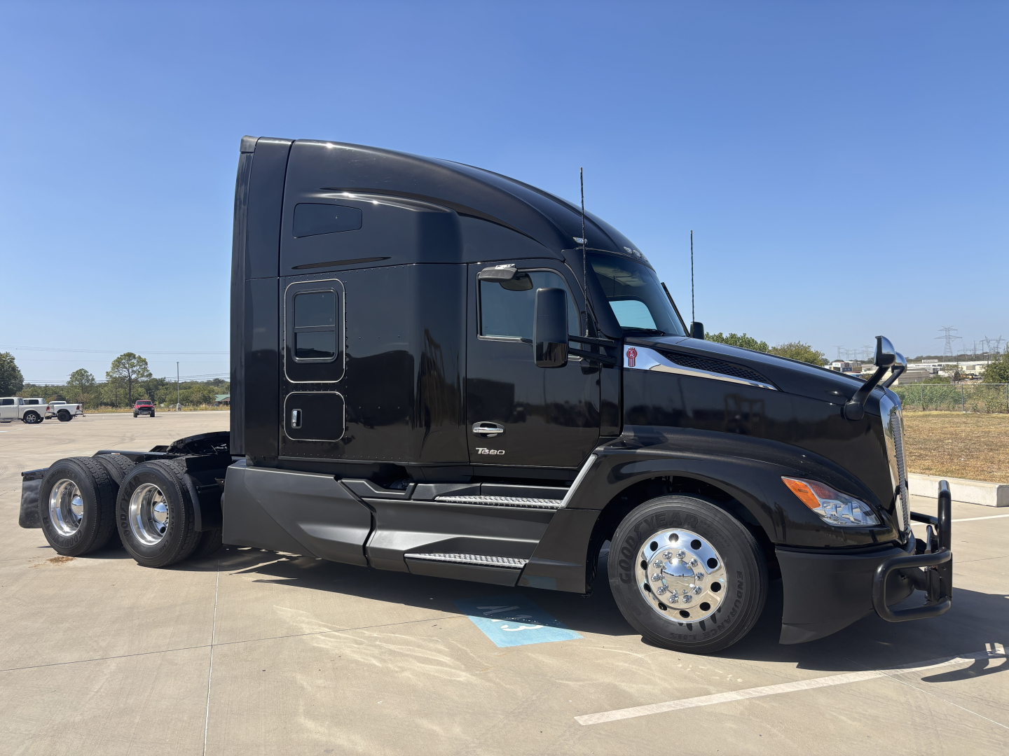 Kenworth T680 semi-truck side profile, black cab, chrome wheels, spare fuel tanks visible, no visible text on side.