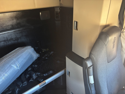 Kenworth T680 cab interior showing sleeper area with mattress and side panel; small storage cabinet; gray seating visible.