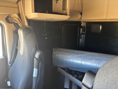 Truck cab interior with driver seat, overhead storage, and a wrapped item in sleeper area. No visible brand text legible.