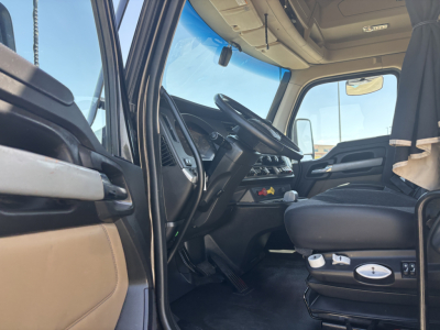 Kenworth T680 truck interior showing steering wheel, dashboard, driver seat with controls; front cabin with beige and black trim, side window, and gear shifter.