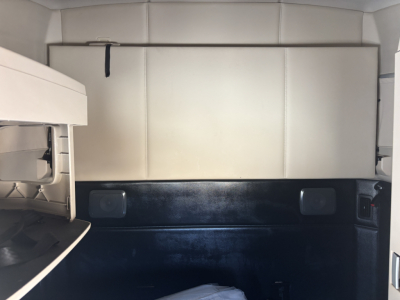 Kenworth T680 sleeper cab interior cargo area with light-colored panels and black lower wall; storage compartments visible.