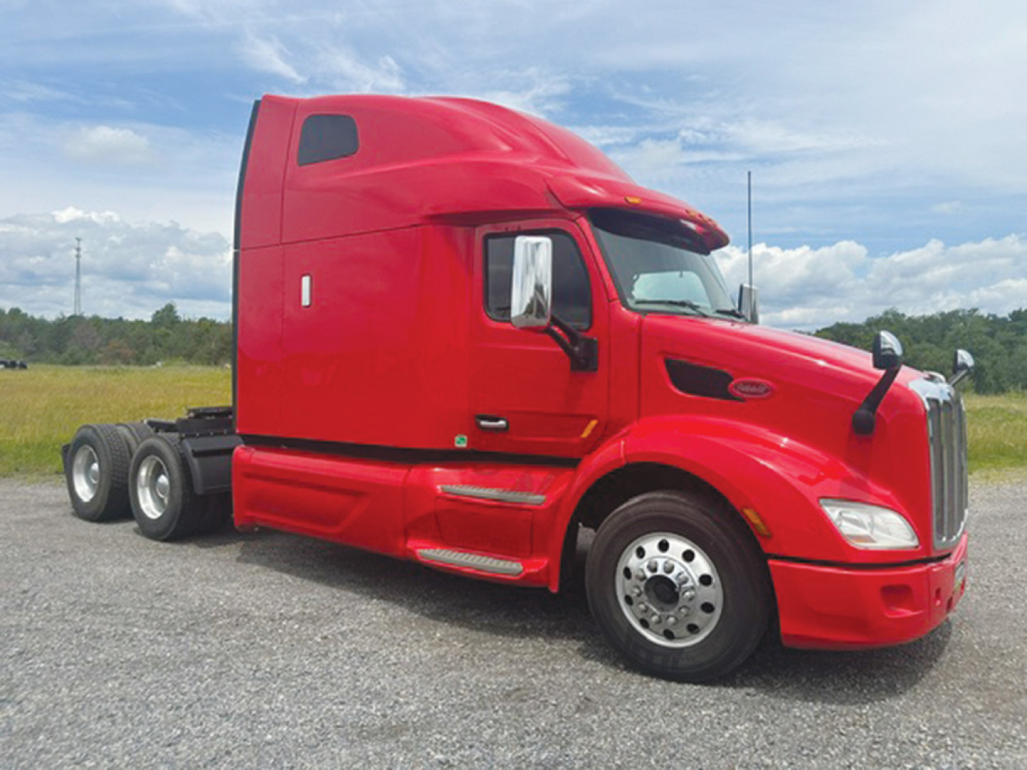 Peterbilt 579 tractor unit in red, side view showing sleeper cab, front grille, large fuel tanks, and dual rear axles.