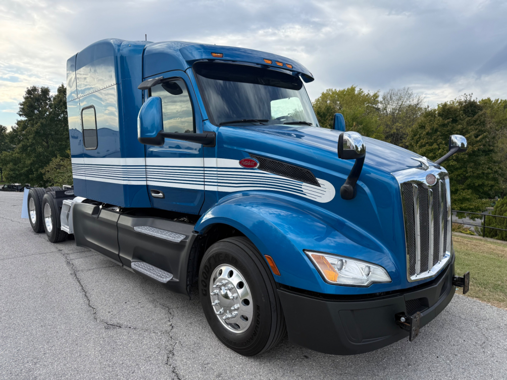 Peterbilt 579 truck in blue exterior showing chrome grille and sleeper cab, side decals, dual rear axles, and chrome wheels.
