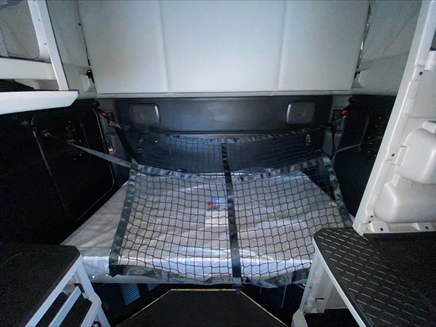 Truck cab interior showing storage area with a cargo net over a metallic mattress/cover; cabin walls and floor panels visible.