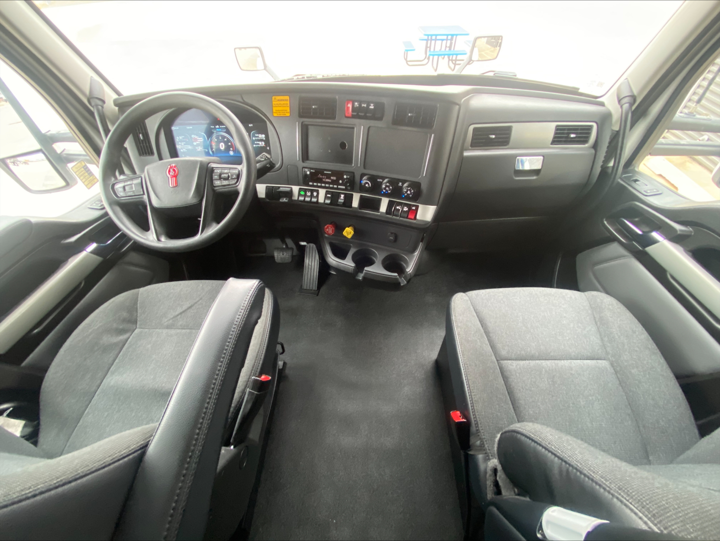 Kenworth T680 interior dash and seating view showing steering wheel, dashboard controls, and two front seats.