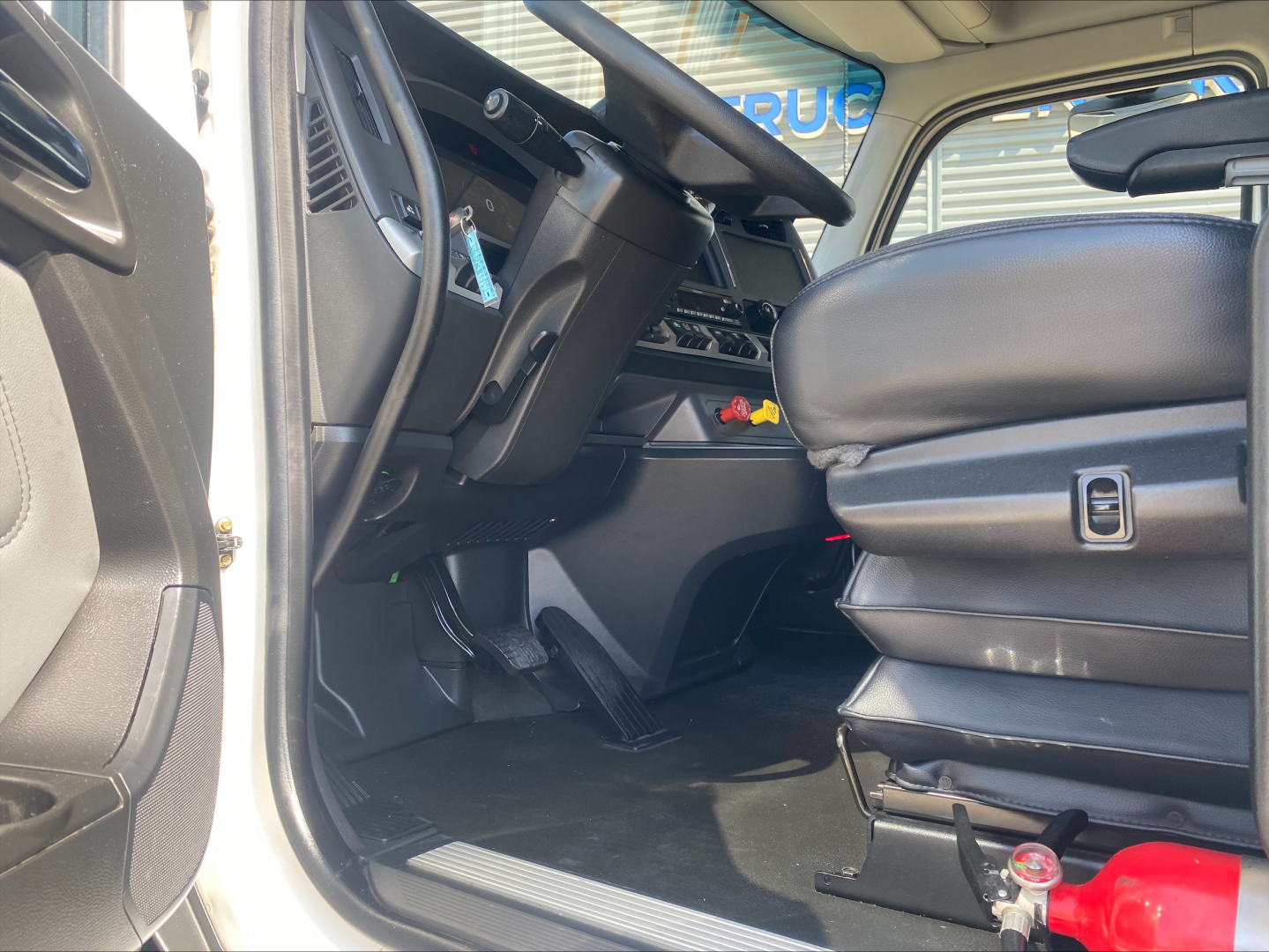 Kenworth T680 cab interior showing driver seat, steering wheel, dashboard and pedals.