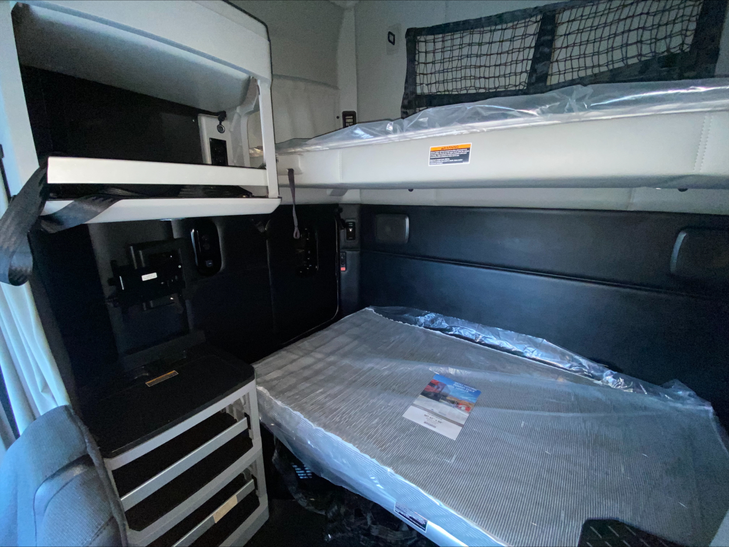 Kenworth T680 sleeper cab interior showing bunk bed area and upper storage cabinet.
