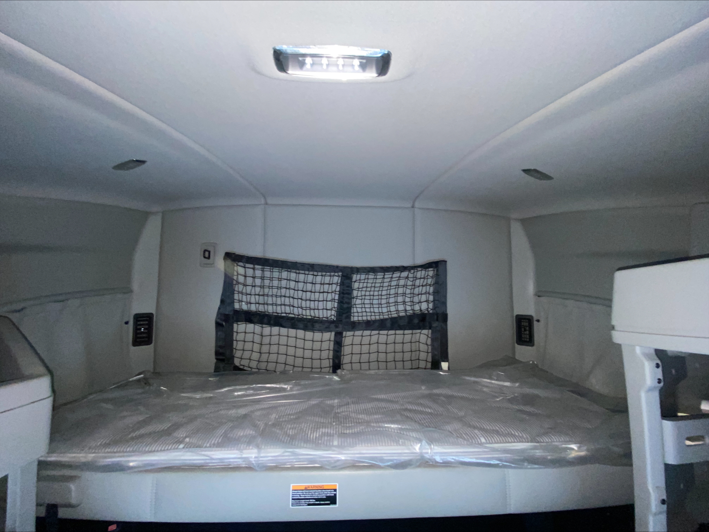 Kenworth T680 sleeper cab interior rear cargo area with a netted barrier and overhead cabin light.