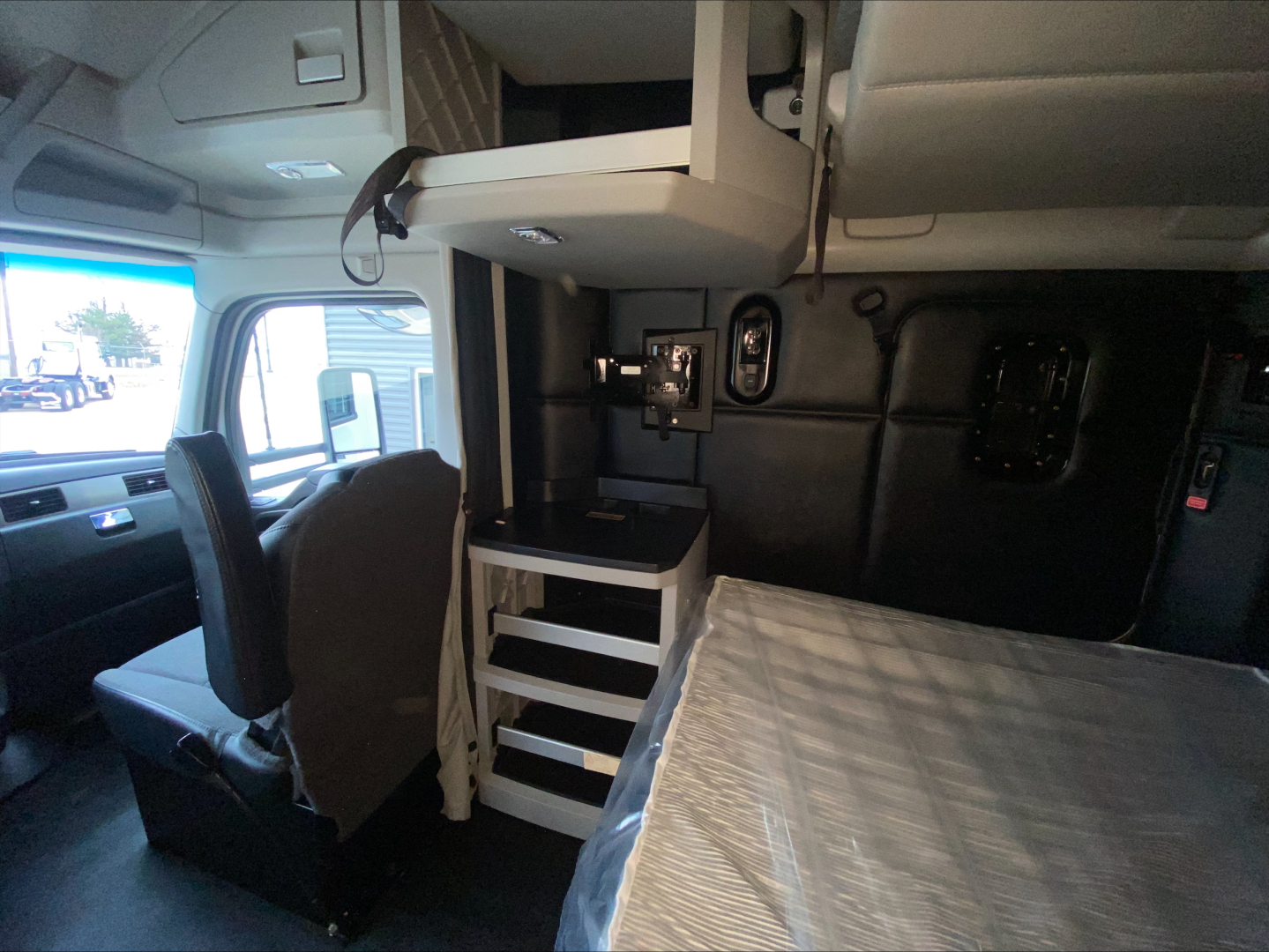 Kenworth T680 truck interior showing sleeper cab with upper bunk storage, small workstation with drawers, and front seating area.
