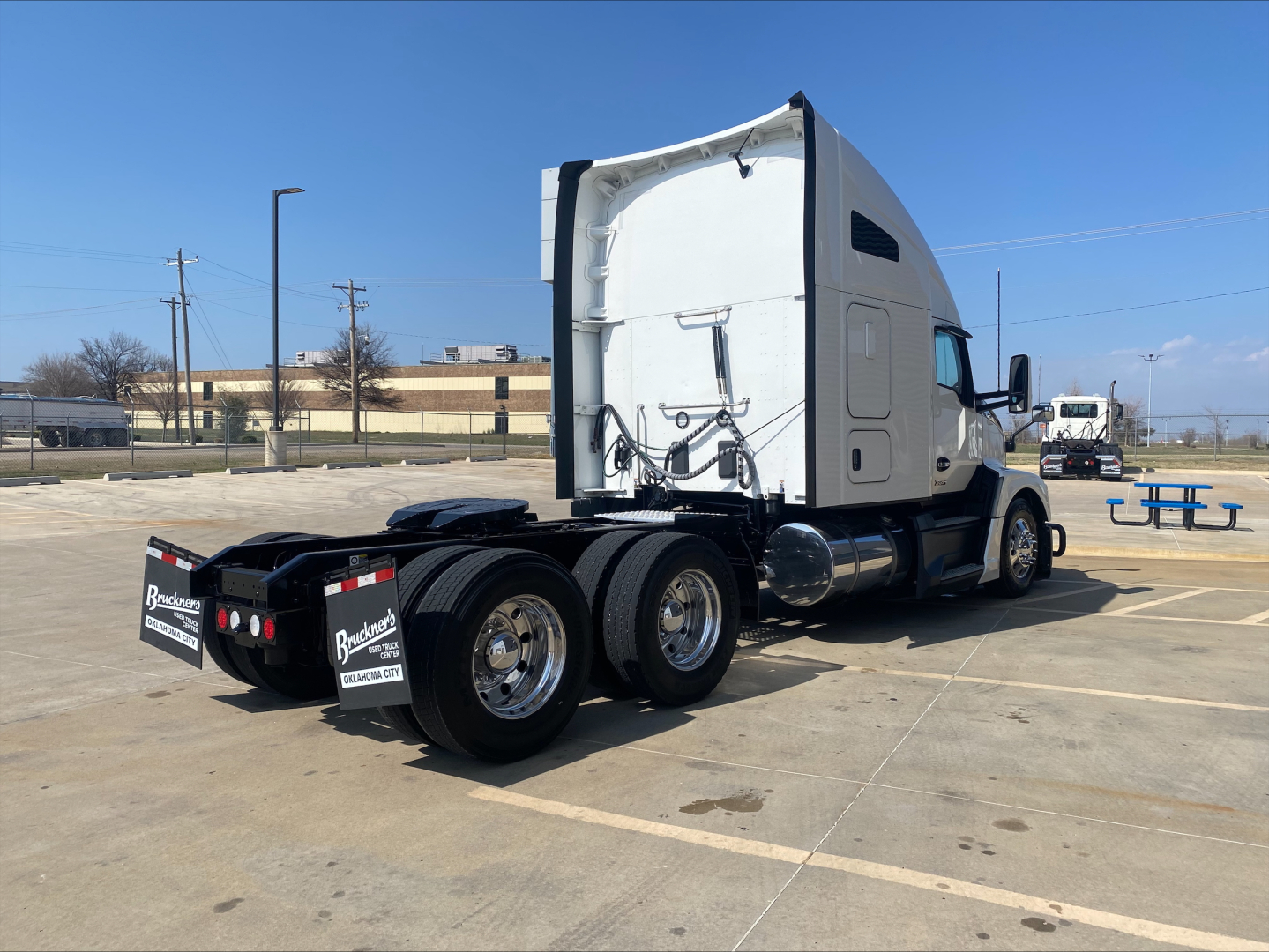 Kenworth T680 tractor in a parking lot, side rear view showing quad rear axles, sleeper cab, and chrome wheels.