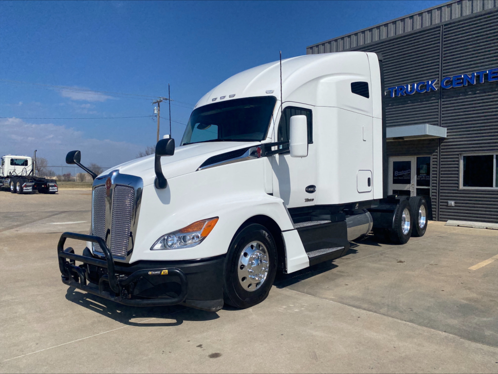 Kenworth T680 conventional sleeper truck in white, front driver-side view, with grille guard, parked outside a truck center.