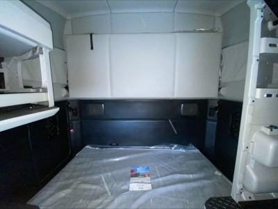 Kenworth T680 truck cab interior cargo area with white storage box above and black lower panels; plastic-wrapped mat on floor; small brochure in the center.