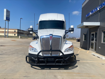 Front view of a white 2023 Kenworth T680 truck with a heavy-duty grille guard in a dealership lot.