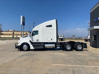 Kenworth T680 tractor in a lot, side view showing sleeper cab, white exterior, tandem rear axles, fuel tanks, and aerodynamic profile.