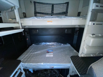 Kenworth T680 truck interior showing sleeper berth area with plastic-wrapped mattress, storage compartments on both sides, and a bed behind the cab.