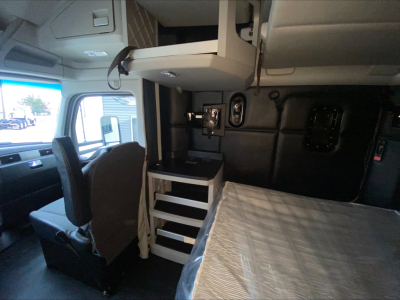 Kenworth T680 truck interior showing sleeper cab with upper bunk storage, small workstation with drawers, and front seating area.