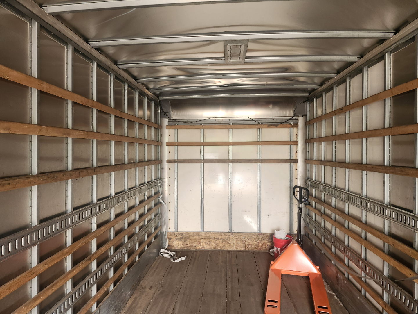 Truck box interior showing metal walls with wooden slats, a small pallet, and a hand truck near the back wall.