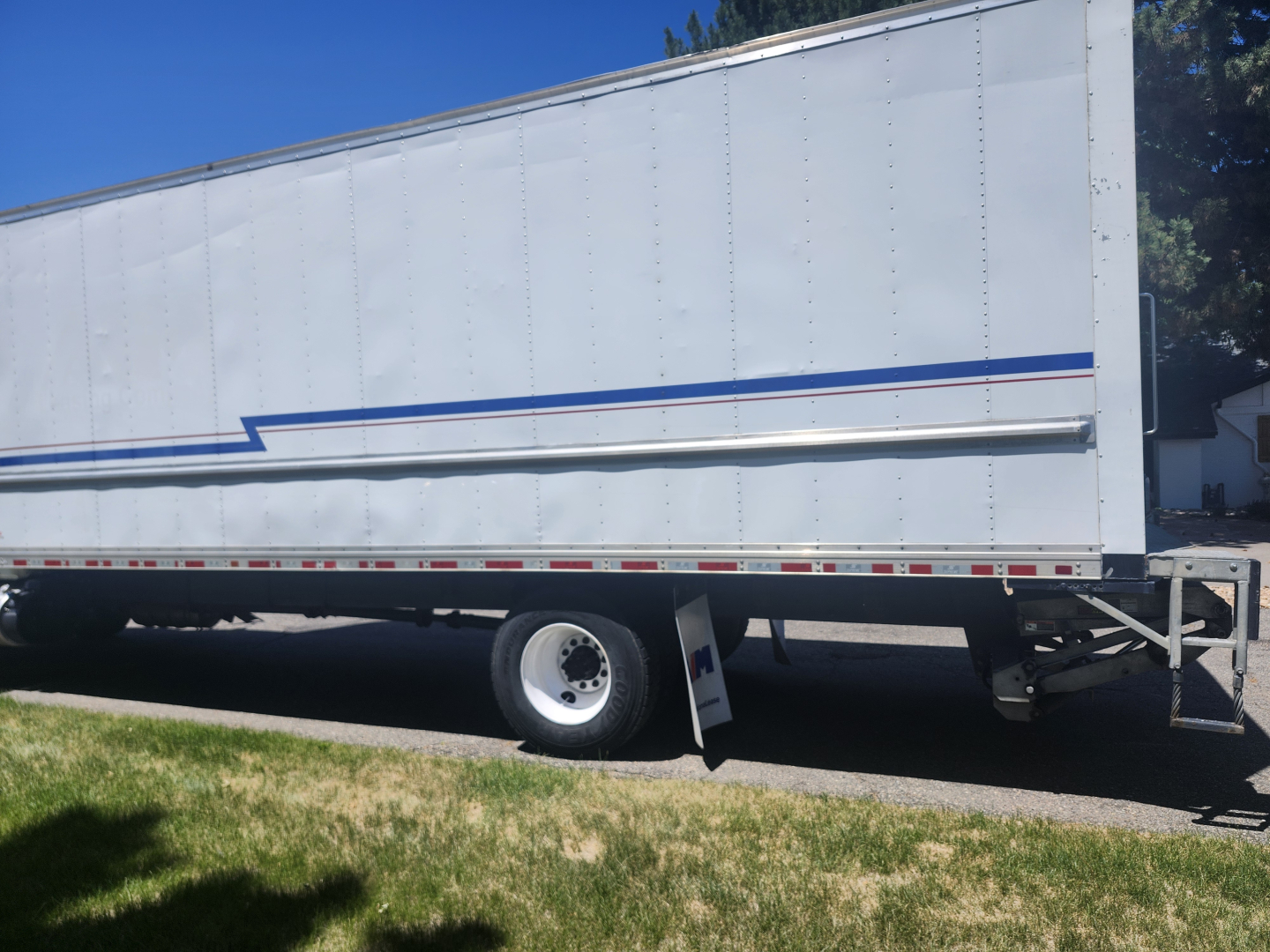 Box truck side view showing large cargo trailer with white siding and blue stripe; front wheel and landing gear visible; VIN and model not shown.
