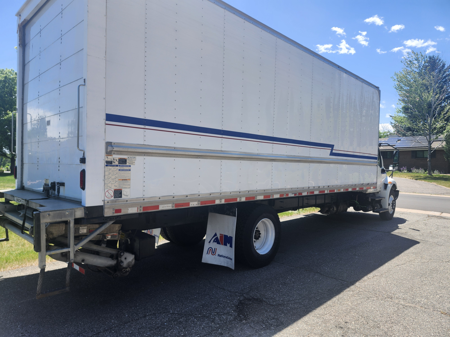 Truck trailer side view of a 2020 International MV607 box truck, white with blue/red stripes, dual rear wheels, license plate not visible.
