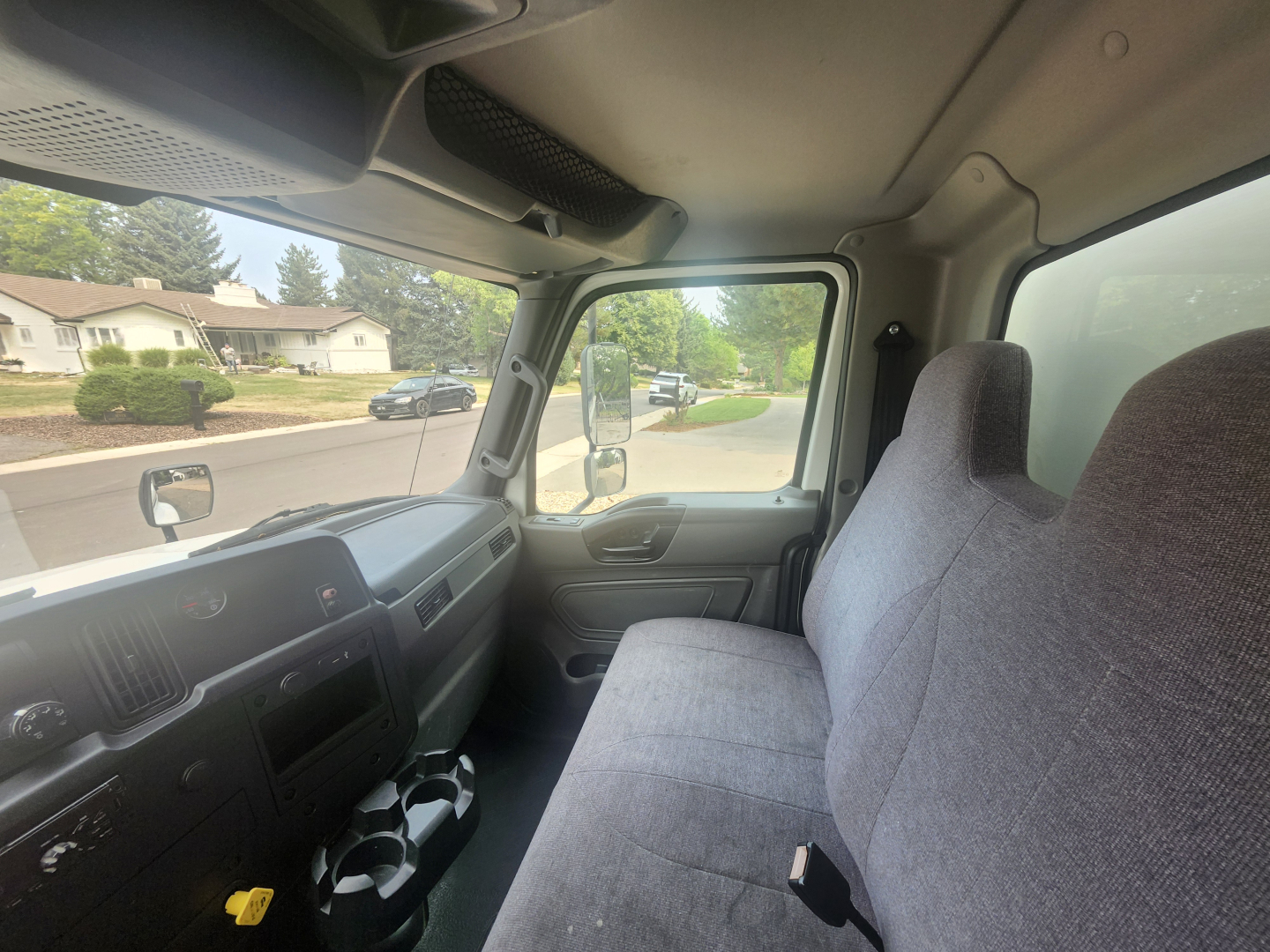 Truck cab interior showing windshield, dashboard, and front bench seat with gray upholstery.