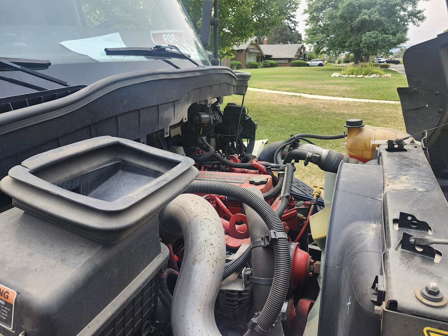 Truck engine bay showing International MV607 with exposed red engine components, hoses, and coolant reservoir visible