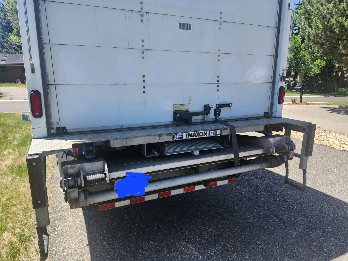 Back view of a 2020 International MV607 truck showing a Maxon hydraulic lift or hitch mechanism and rear bumper, with reflective red-and-white tape along the lower edge.