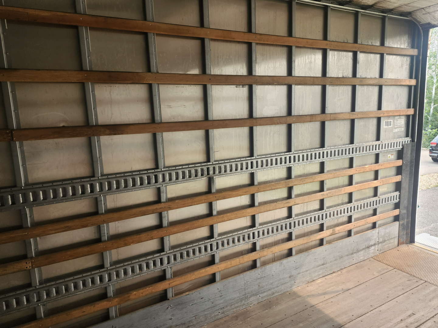 Trailer interior showing metal side rails and wooden planks in a box truck cargo area.