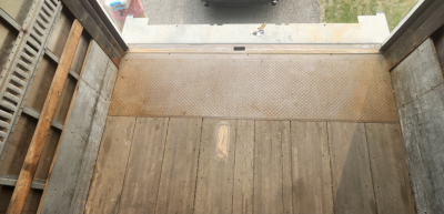 Truck box interior view showing wooden floor planks and metal threshold, from a raised vantage inside the cargo area.