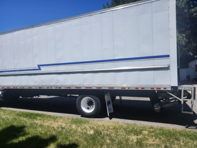 Box truck side view showing large cargo trailer with white siding and blue stripe; front wheel and landing gear visible; VIN and model not shown.
