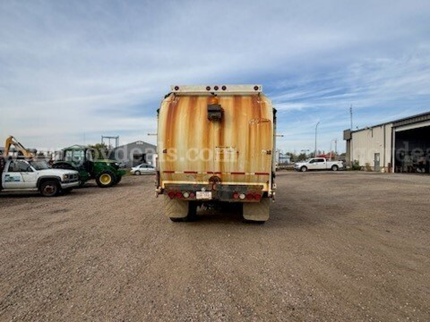 Rear view of a weathered garbage truck with tan body in a dusty lot.