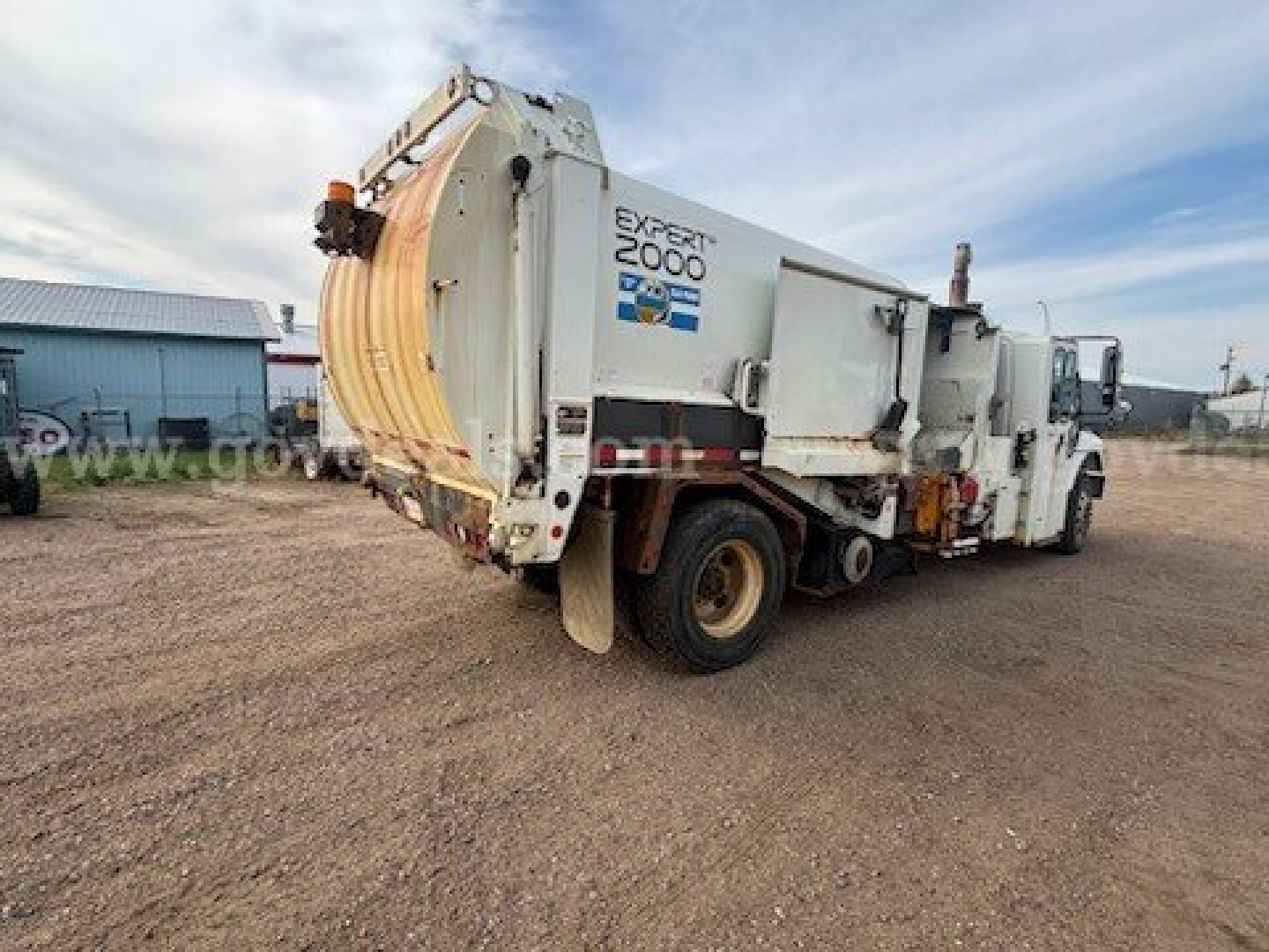 Garbage truck in a yard showing mid-section with 'EXPERT 2000' label and various utility panels on white body.