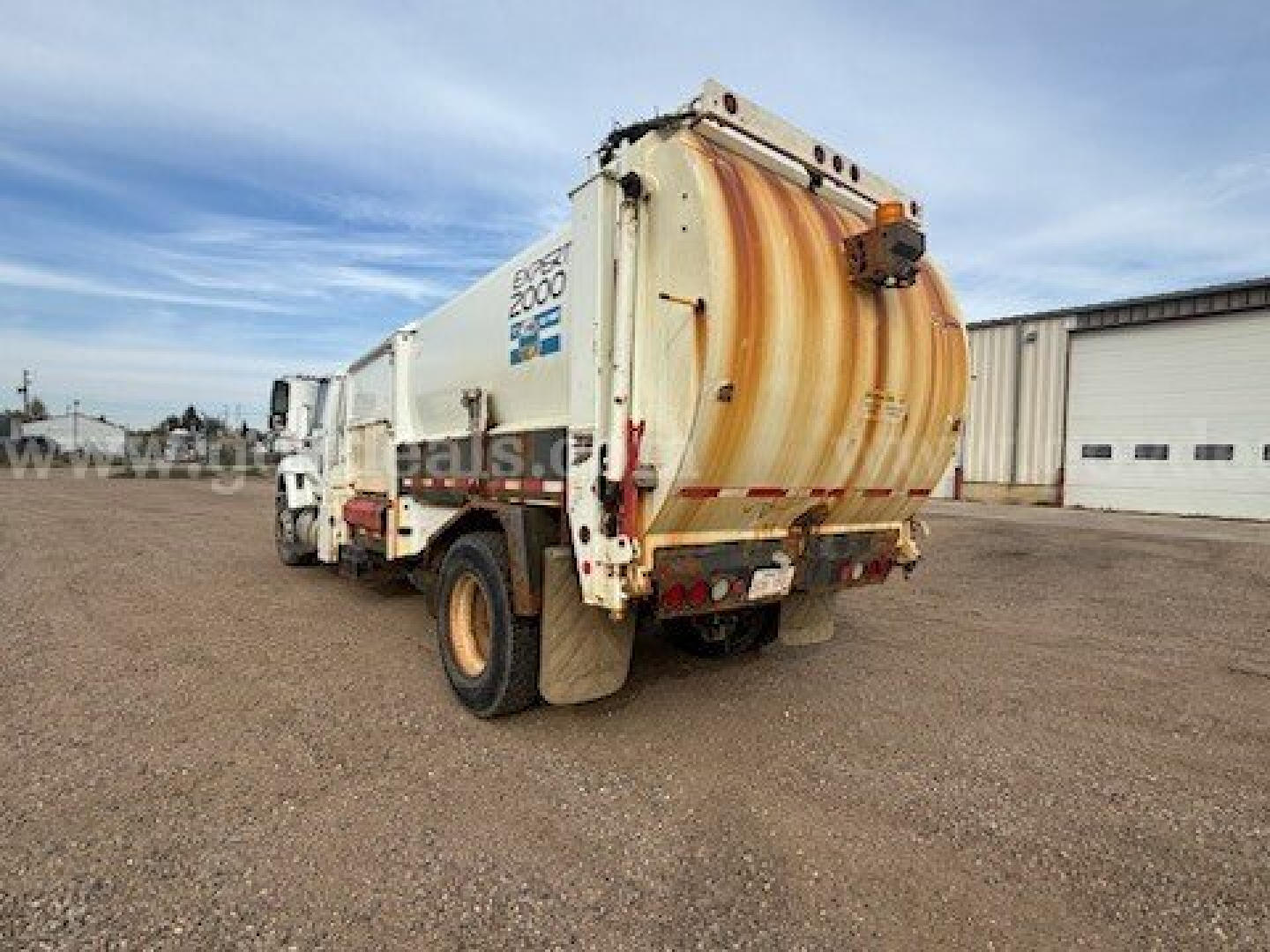Rear/side view of an International 7400 garbage truck showing a large cylindrical rear compactor with rust-colored rear hatch and 'EAST 2000' label on side; truck body and wheels visible.