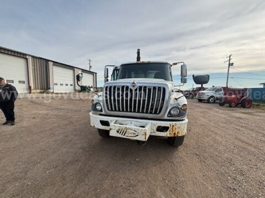 Front view of a white International 7400 truck with large grille, bumper, and two side mirrors; dirt/grime on bumper area; diesel truck in a yard.