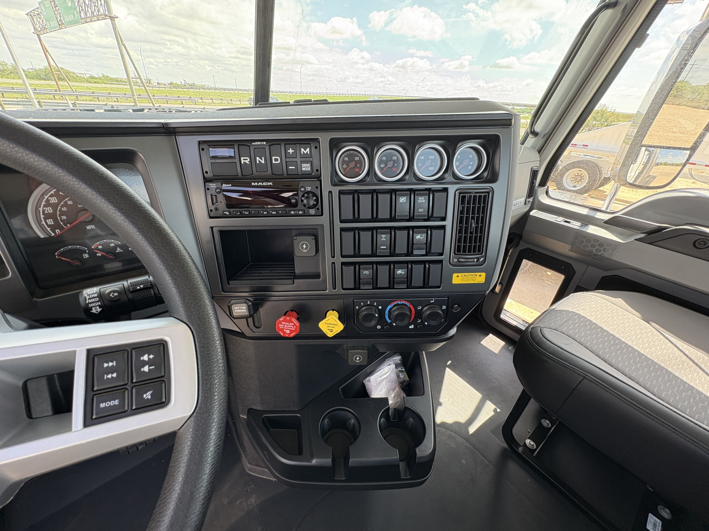 Dashboard of a 2027 Mack PI64T truck cab showing gauges, controls, and steering wheel; HVAC and radio area visible.
