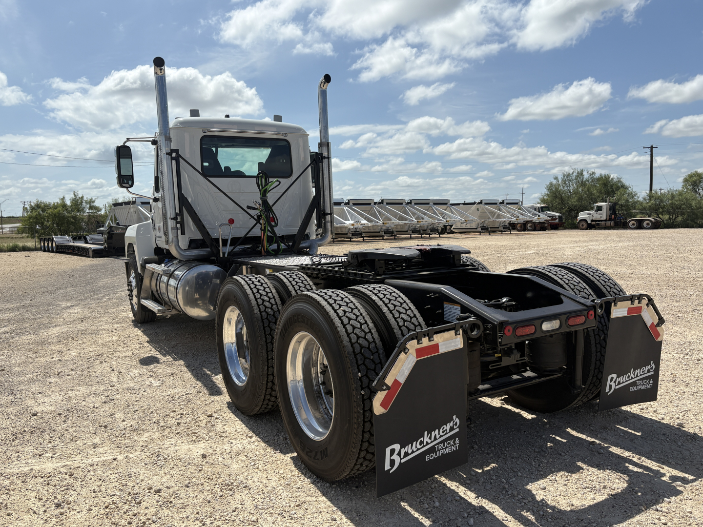 Mack PI64T truck tractor rear view showing dual rear axles, mud flaps with Buckner's logo, fuel tanks, and fifth wheel hardware.