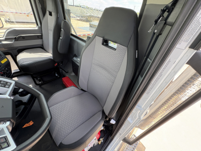  cockpit of a 2027 Mack PI64T truck showing grey fabric driver seat and part of the dashboard.