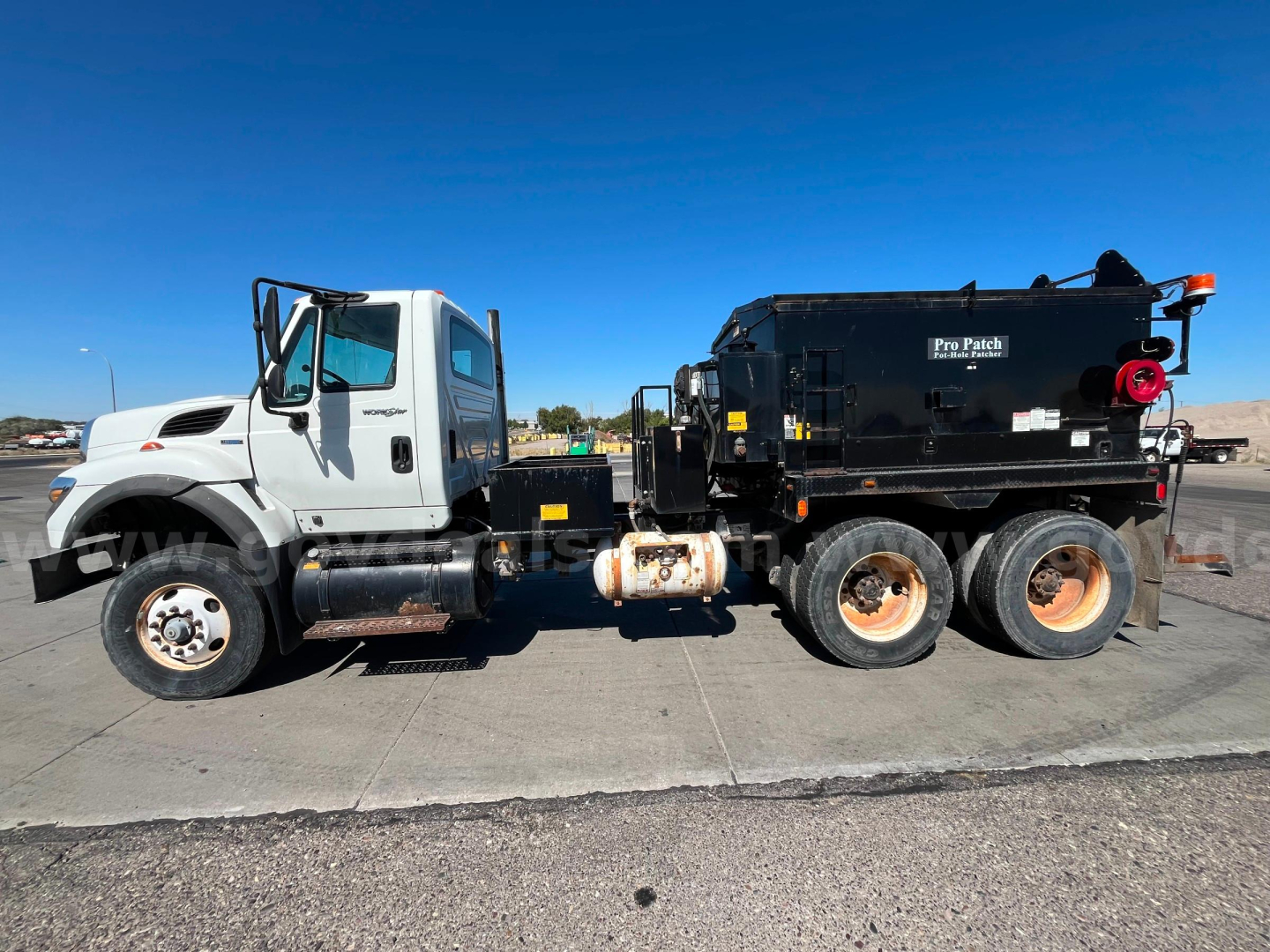 Truck side view of 2011 International WorkStar 7600 asphalt hot oil truck with Pro-Patch body and black tank; visible VIN tag and stock number in listing.