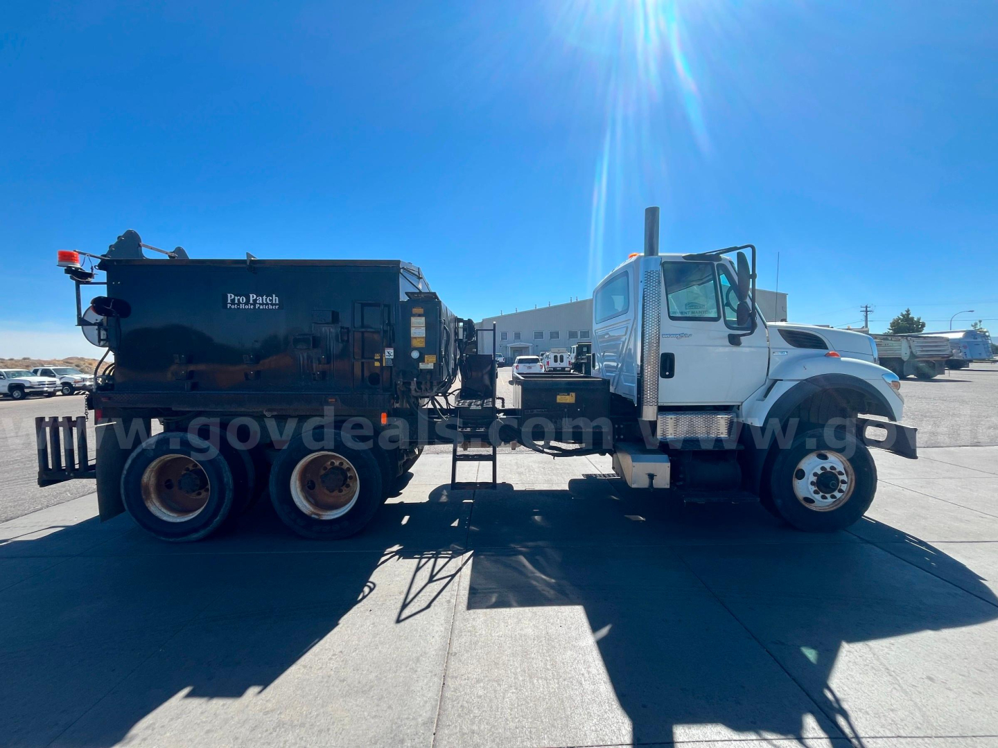 Truck-mounted asphalt heater body attached to International WorkStar 7600 cab and chassis, side view, white cab, black asphalt heater unit, dual rear axles.