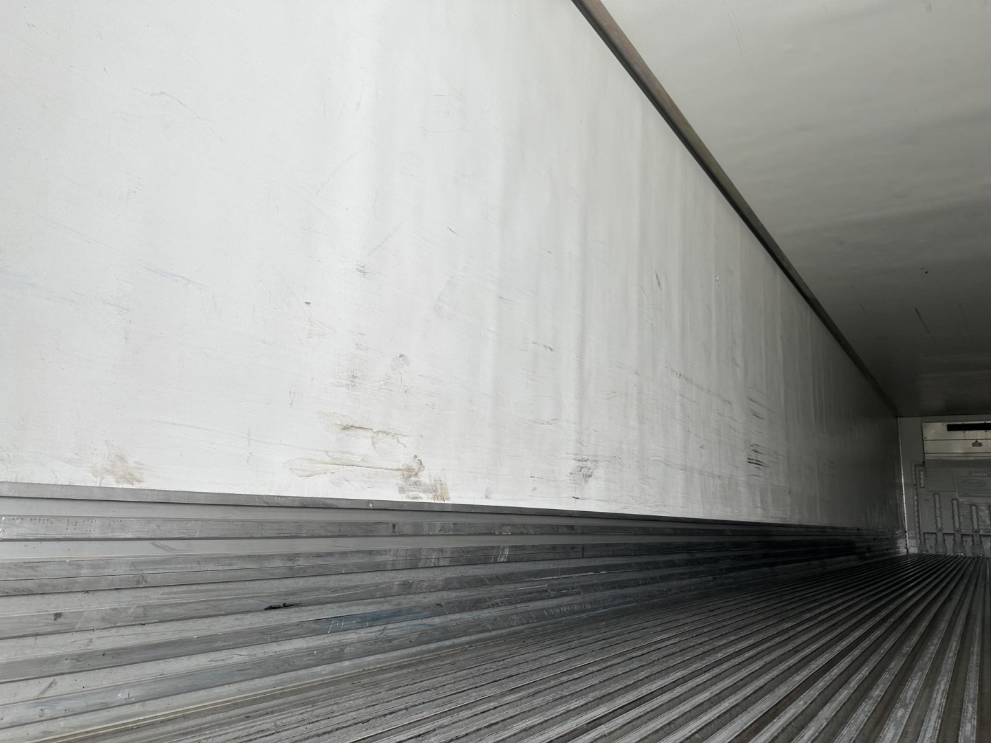Trailer interior showing corrugated metal floor and sidewalls with faint marks and a small white unit at far end.