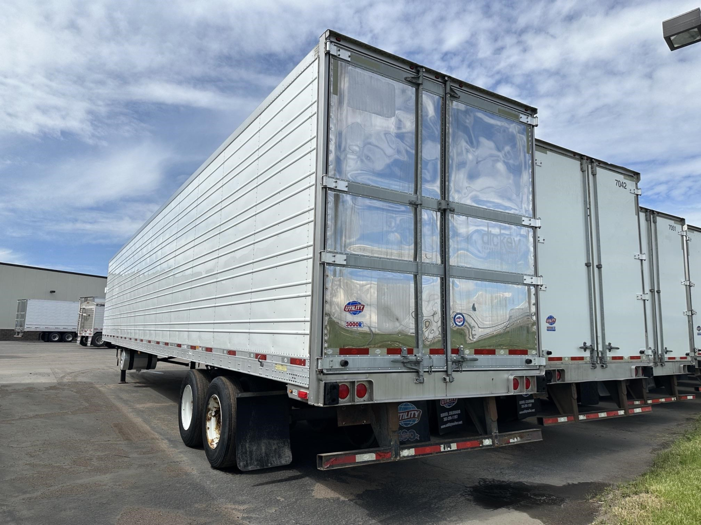Utility 3000R trailer in a storage lot, rear view with double doors, tandem axles, metal siding, and reflective safety markers.